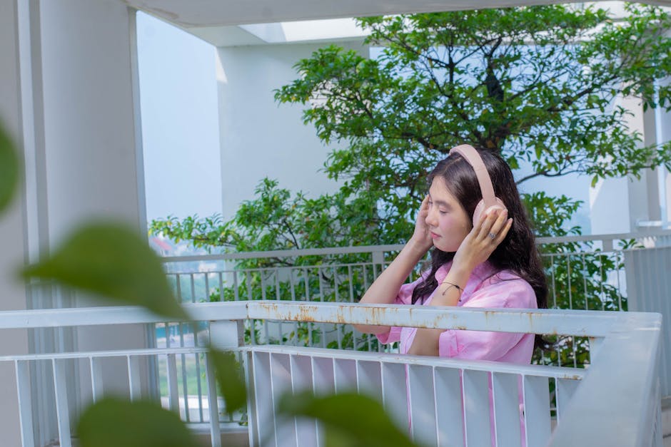 Seseorang sedang mendengarkan musik menggunakan headphone dengan ekspresi wajah yang tenang dan damai di lingkungan asri.